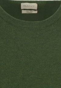 Groene gebreide trui met een ronde halslijn, voorzien van een ribbeltextuur en een label dat het merk "GANT" en materiaaldetails aangeeft.