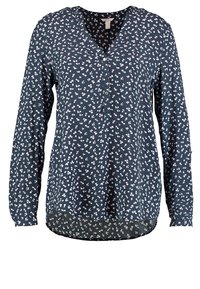Blouse à manches longues bleu marine avec une patte de boutonnage, présentant un motif floral rose et blanc, confectionnée en tissu léger, avec un ourlet arrondi.