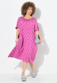 Abito rosa con una silhouette ampia a forma di A, maniche corte e un motivo sottile. Abbinato a sandali con piattaforma di un blu chiaro e una clutch coordinata.