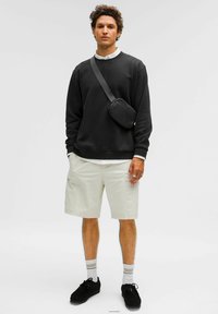 Felpa nera, pantaloni cargo crema, sneakers nere e calzini a righe. Include una borsa a tracolla nera. Texture semplici senza motivi.