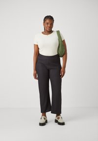 Ribbed white t-shirt, textured dark pants with a geometric pattern, and green quilted shoulder bag. Chunky white shoes with black sole.