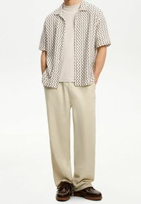 Kortärmad skjorta i krämfärgad med svart zigzag-mönster, kombinerad med ljusbeige byxor och bruna skor, med en avslappnad passform.