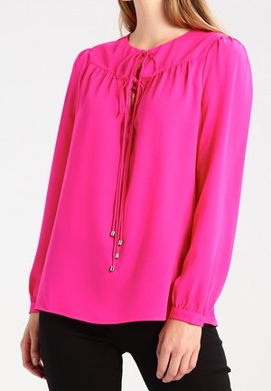 Blusa rosa brillante in tessuto leggero, con maniche lunghe, scollatura rotonda e un dettaglio con fiocco davanti arricchito da elementi metallici.