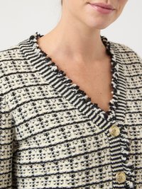 Sweter kardigan w kremowym i czarnym kolorze z poziomymi paskami, z dekoltem w serek, falbankami na krawędziach oraz złotymi guzikami. Całość zdobi teksturowany wzór.