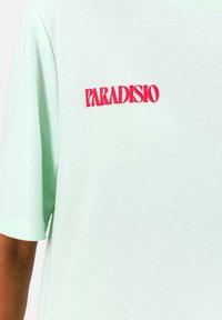 Camiseta de algodón verde claro con un prominente estampado rojo "PARADISIO". Diseño de manga corta y cuello redondo con una textura suave.