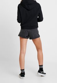 Sudadera corta negra con capucha, combinada con pantalones cortos de mezclilla gris oscuro y zapatillas negras con acentos blancos. Medias a rayas blancas y negras.