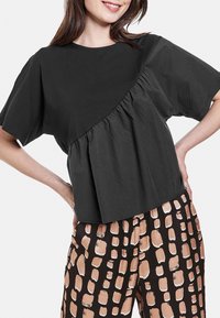 Top corto negro con escote redondo y mangas cortas, con tejido recogido en un lado y silueta en A.