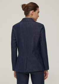 Blazer in denim navy con una vestibilità sartoriale, revers a punta, spacco singolo sul retro e una texture sottile. Maniche lunghe con cuciture pulite.