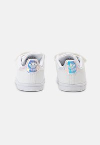 White leather sneakers with flat laces, padded collar, and iridescent accents on heel tab featuring the "Stan Smith" logo.