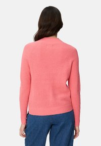 Rosa gerippter Pullover mit langen Ärmeln, rundem Ausschnitt und tailliertem Schnitt. Weiche Textur und minimalistisches Design betonen das gemütliche Erscheinungsbild.