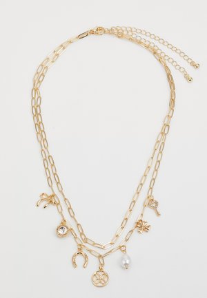 Collar de capas en tono dorado que presenta diversos charms: una perla, una llave, un herradura, un lazo, un cristal y detalles de trébol; diseño con cadena de eslabones alargados.