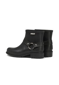 Bottes de pluie noires à chevilles avec semelles épaisses, sangles en cuir décoratives, anneaux en métal et patchs de logo AIGLE sur fond blanc.