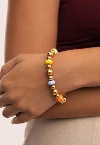 La pulsera de cuentas presenta esferas doradas brillantes intercaladas con cuentas de colores pastel en tonos amarillo, verde, azul, naranja y rosa.