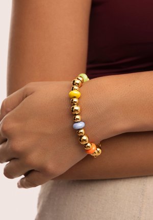 La pulsera de cuentas presenta esferas doradas brillantes intercaladas con cuentas de colores pastel en tonos amarillo, verde, azul, naranja y rosa.