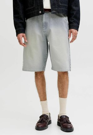 Férfi világosra mosott csíkos rövidnadrágban, sötétbarna bőr bojtos mokaszinban, krémszínű zokniban és sötét farmerdzsekiben.