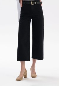 Czarne krótkie dżinsy z wysokim stanem i szerszym krojem, połączone z czarnym paskiem z złotą klamrą i beżowymi butami na słupku.