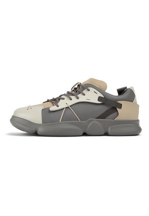 Zapatilla baja con paneles grises, beige y blancos, cordones negros y una suela gruesa y texturizada en gris, mostrada desde el lado exterior.
