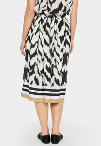 Rochie cu model alb și negru, cu un design plisat, prezentând un tiv solid în dungi alb-negru și un accent bej în partea de jos.