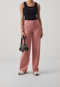 Top in tessuto a coste nero, pantaloni su misura rosa chiaro, e una piccola borsa nera. I pantaloni sono a gamba larga e le scarpe sono beige con dettagli crema.