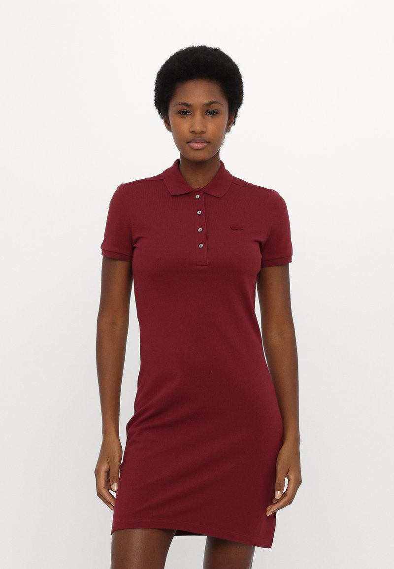 Robe polo bordeaux à manches courtes, avec patte de boutonnage et texture côtelée. Présente un petit logo brodé sur la poitrine.