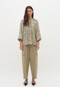 Khaki oversized särk valge abstraktse printimisega, mida täiendab lahtised khaki cargo püksid küljetaskutega, koos mustade terava ninaga kortsekingadega.