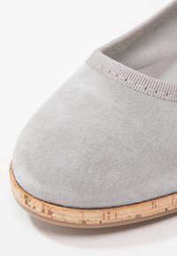 Ballerine en suède gris avec un bout arrondi, dotée d'une bordure élastique gris clair et d'une semelle en liège texturée. Design épuré et minimaliste.