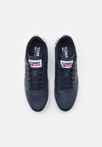 Sneakers blu navy con tomaia in pelle liscia, suola in gomma bianca, punta tonda e lacci tono su tono. Presenta il logo "TOMMY JEANS" sulla linguetta.