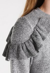 Grauer Strickpullover mit strukturiertem Stoff und Rüschendetails an den Schultern. Klassischer Rundhalsausschnitt und körpernahe Passform.