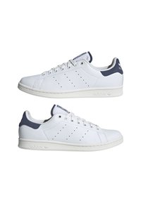 Coppia di sneakers Adidas Stan Smith bianche con talloni blu navy, strisce traforate e suole in gomma bianca, viste di lato.