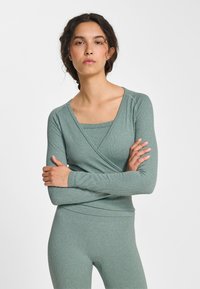 Top met lange mouwen en wikkelstijl van gestructureerde, gedempte groene stof, gecombineerd met een bijpassende strakvallende laag eronder.