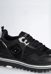 Zapatilla negra con cuero perforado, suela gruesa con rayas blancas, cordones negros y marca Liu Jo en la suela y la lengua.