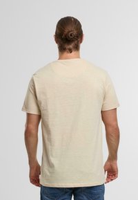 Beige short-sleeved t-shirt made of soft fabric, featuring a round neck, and a slightly heathered texture. Visible stitching at the hem.