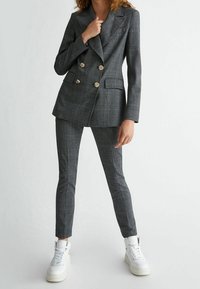 Szary w kratę dwurzędowy blazer z złotymi guzikami, zestawiony z dopasowanymi spodniami i białymi sneakersami, z teksturowanym wykończeniem materiału.