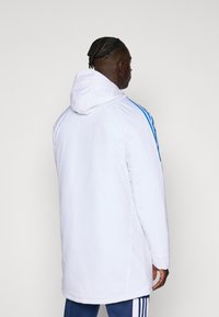 White hooded parka with blue stripes, featuring a smooth texture and a longer cut, designed for warmth and comfort.