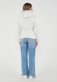 Giacca imbottita grigia chiara con cappuccio e cuciture orizzontali, abbinata a jeans a gamba larga blu sbiaditi e sneakers bianche.