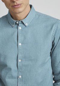 Light blue, button-up shirt made of soft fabric; features a classic collar, white buttons, and a smooth texture.