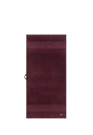 Serviette de bain bordeaux foncé avec des bandes texturées en haut et en bas et un petit logo de crocodile vert près du coin inférieur droit.