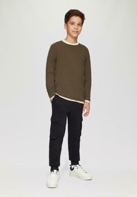 Olijfgroene langemouwshirt met een crèmekleurige kraag, gecombineerd met zwarte cargobroeken met zijzakken, afgewerkt met witte sneakers.
