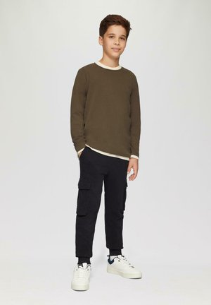 Olijfgroene langemouwshirt met een crèmekleurige kraag, gecombineerd met zwarte cargobroeken met zijzakken, afgewerkt met witte sneakers.