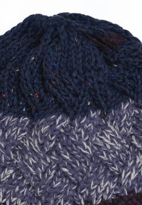 Gebreide beanie in donker marineblauw en paars. Kenmerkt zich door gestructureerde patronen met kleurrijke spikkel van rood en geel. Zachte, dikke vezels.