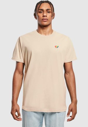 Tricou din bumbac bej, cu mâneci scurte, având un mic design cu inimă multicoloră pe pieptul stâng. Stil clasic cu gât rotund.