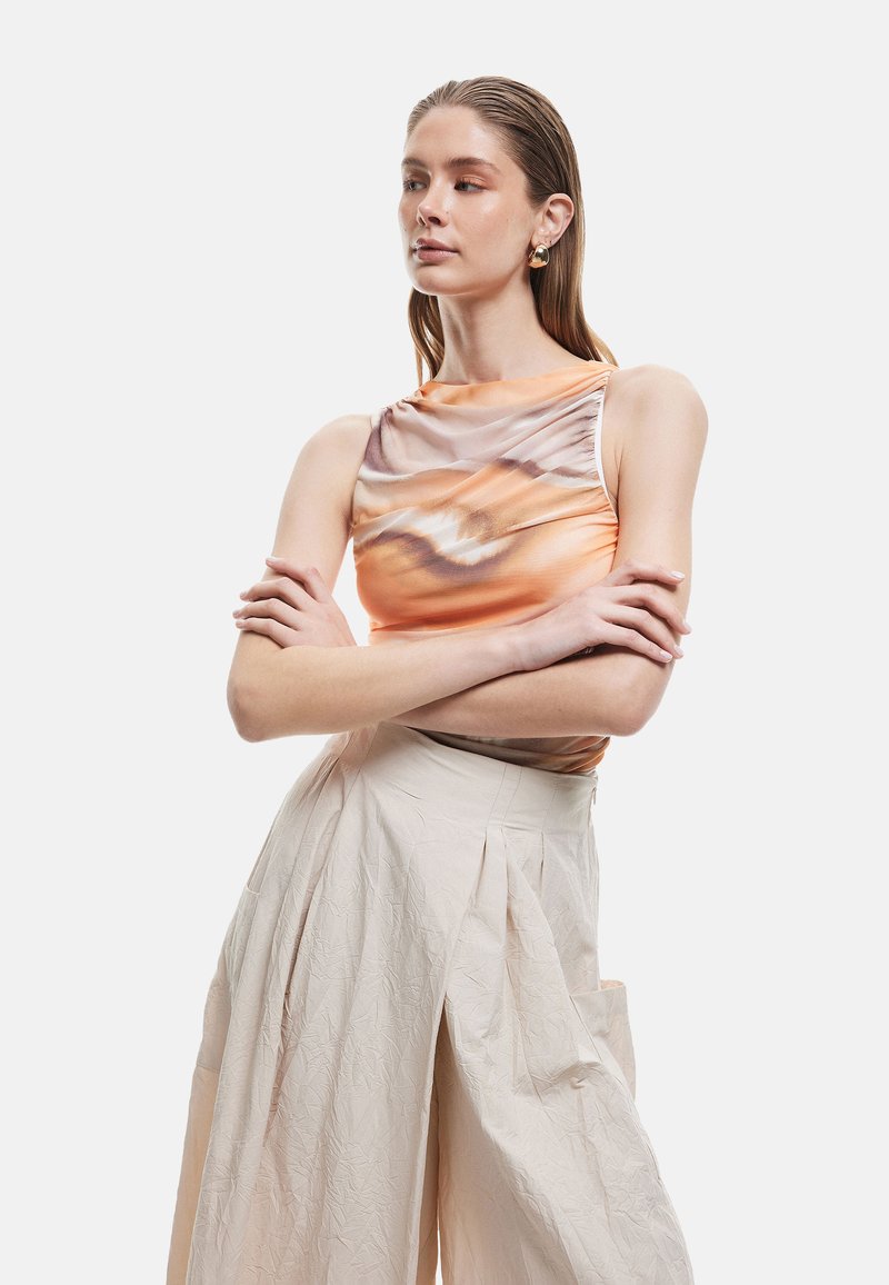 Oranje en beige mouwloos top met een gedrapeerd ontwerp en abstracte patroon, gecombineerd met beige plooibare wijde broek. Gladde textuur.