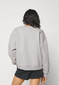 Sudadera gris de manga larga, con cuello redondo y puños acanalados, que presenta un ajuste relajado y corto. Llevada con pantalones cortos negros.