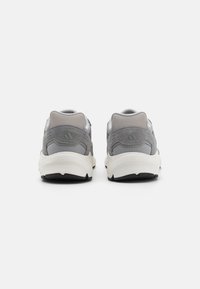 Chaussures de sport grises en matériaux en mesh et en daim, de forme arrondie, avec un col rembourré et des détails de semelle intermédiaire blanche contrastante.