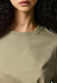 Olivgrön bomullst-shirt med rund halsringning. Tyget verkar mjukt och lätt med korta ärmar och utan synliga mönster.