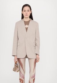 Beige tailored blazer with a notch lapel, two front pockets, paired with patterned skin-toned leggings featuring pink and brown accents.