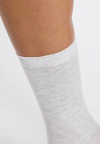 Calcetín de color gris claro, con canalé, hecho de una tela suave y elástica. Presenta un puño doblado en la parte superior y un acabado liso.