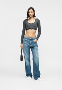 Γκρι cropped μπλούζα με μακριά μανίκια και λωρίδα με λογότυπο· χαλαρά ανοιχτό μπλε τζιν· λευκά αθλητικά παπούτσια· το μοντέλο κρατά μια μικρή μαύρη τσάντα.