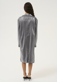 Gray satin long coat with a collar, dropped shoulders, and a sleek finish, featuring a side slit and long sleeves, worn over black heels.