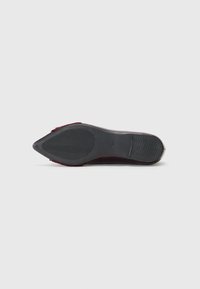 Semelle de chaussure à talon haut en suede rouge, design à bout pointu, semelle extérieure en caoutchouc texturé avec des rainures, et zone de talon plate pour la stabilité.